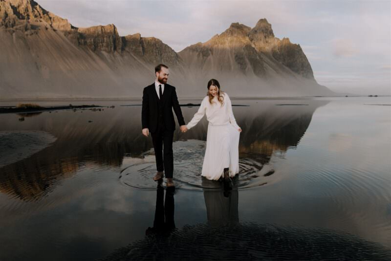 A wedding couple walking on wet sand that mirrors the surroundings.