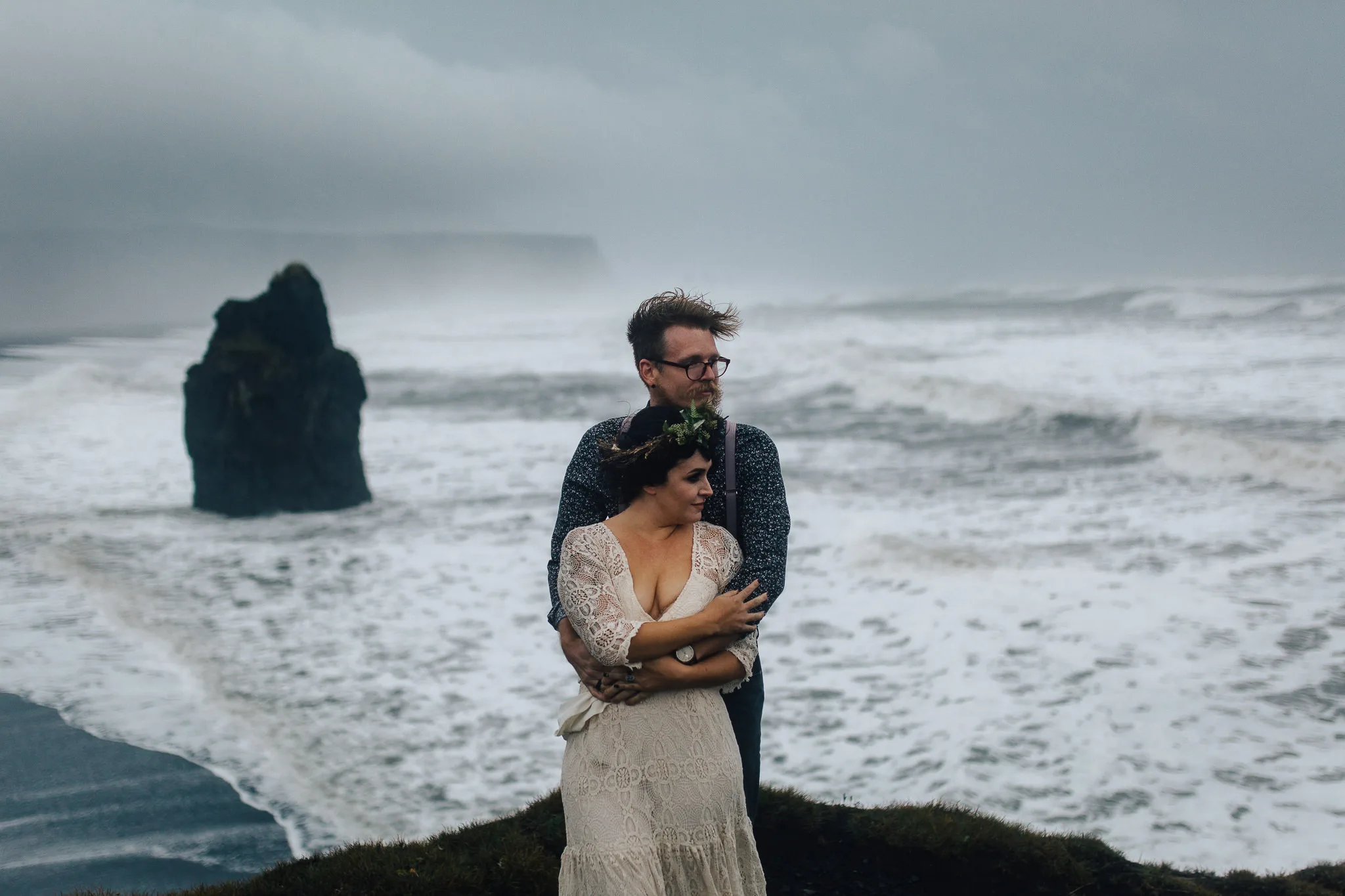 A wedding couple standing in front of a raging sea.