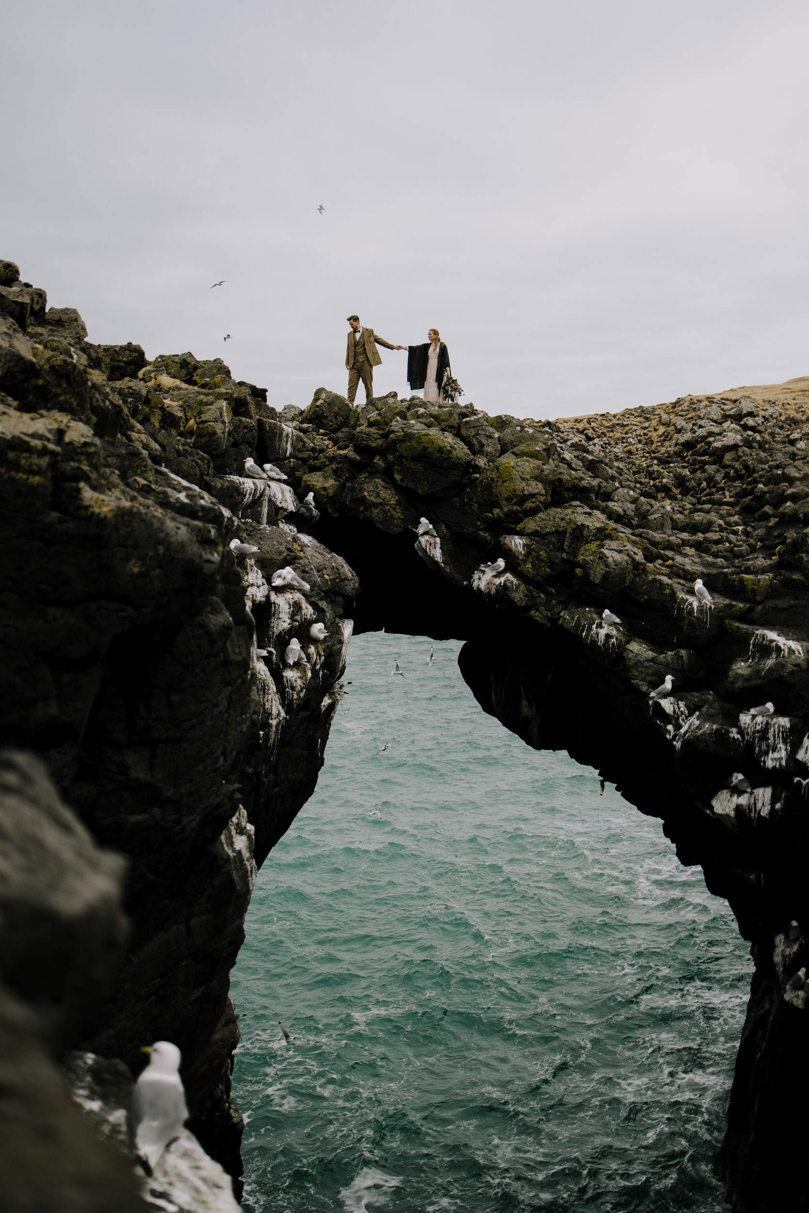 A couple walks over a stone arch on their elopement day in Iceland.