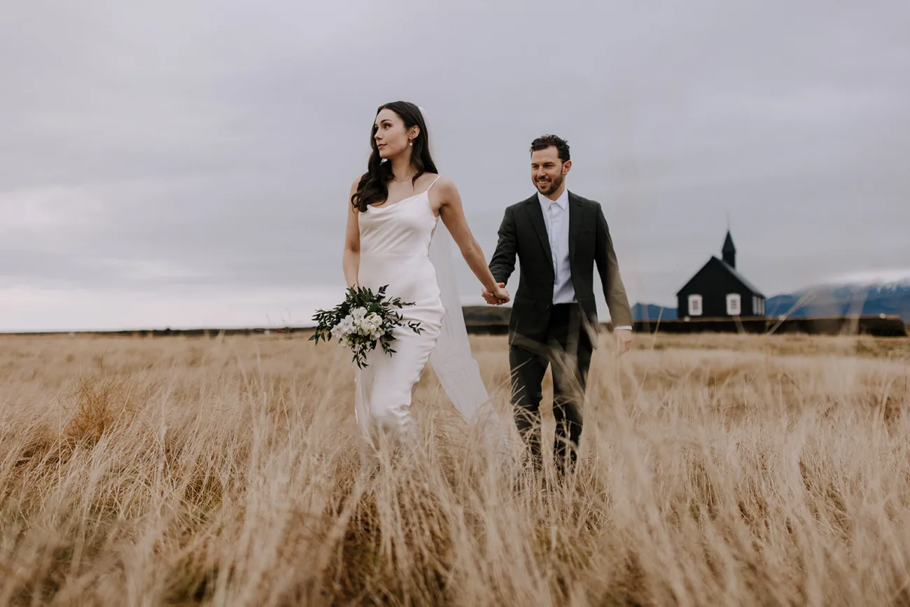 Bride and groom walking from the black church in a yellow field. Bride wearing a silk dress.