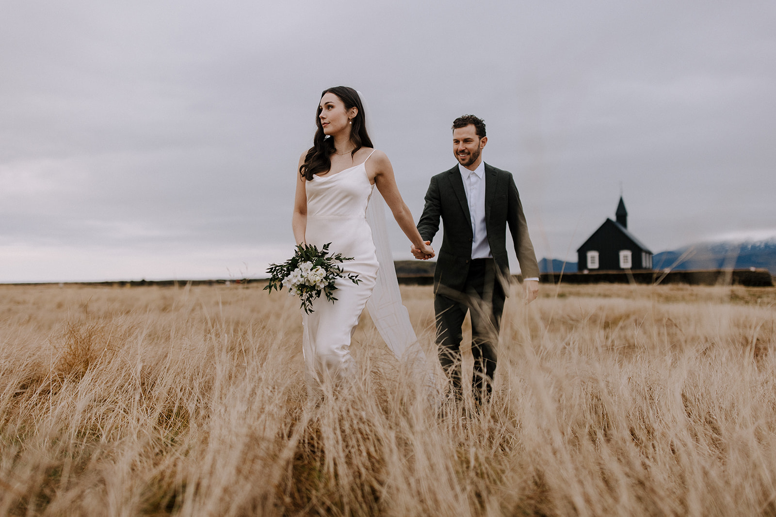 A bride and groom walk through tall grass after their Iceland wedding ceremony.