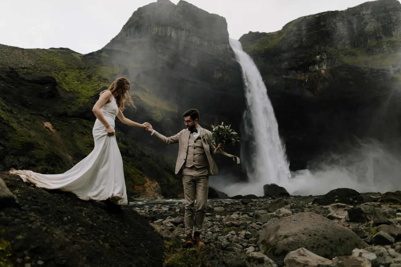 Groom leading his bride towards a majestic waterfall