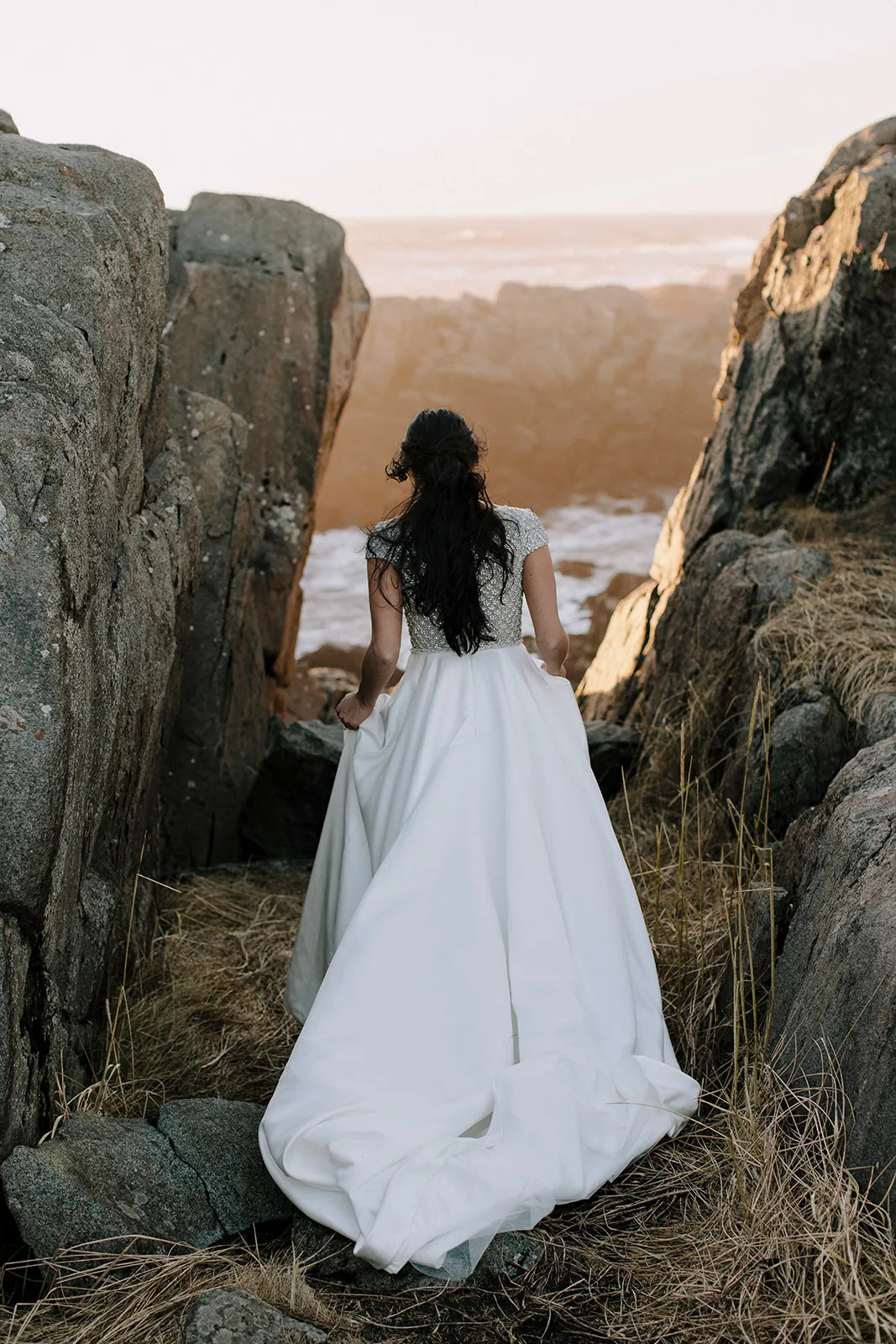 Bride walking away from the camera towards amazing light an an cliff edge