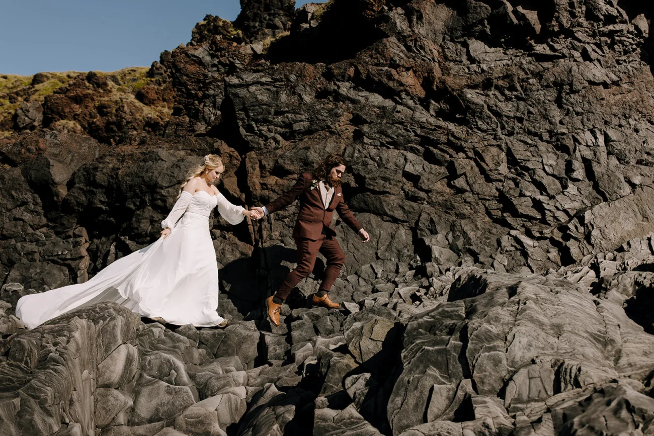 Bride and groom walking through rock formation in their wedding attire