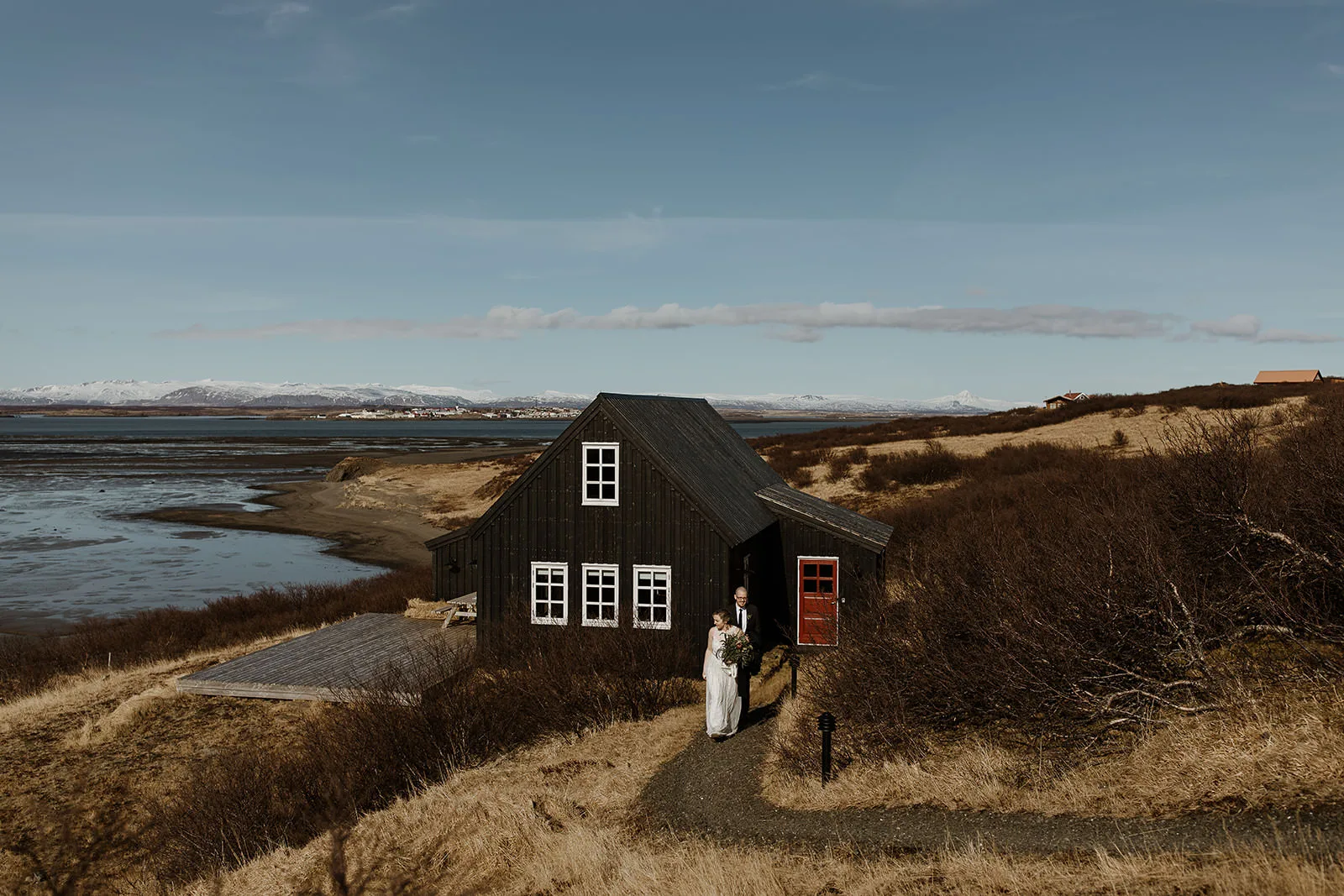 A wedding couple walks from an old black timber house on the west coast of Iceland.