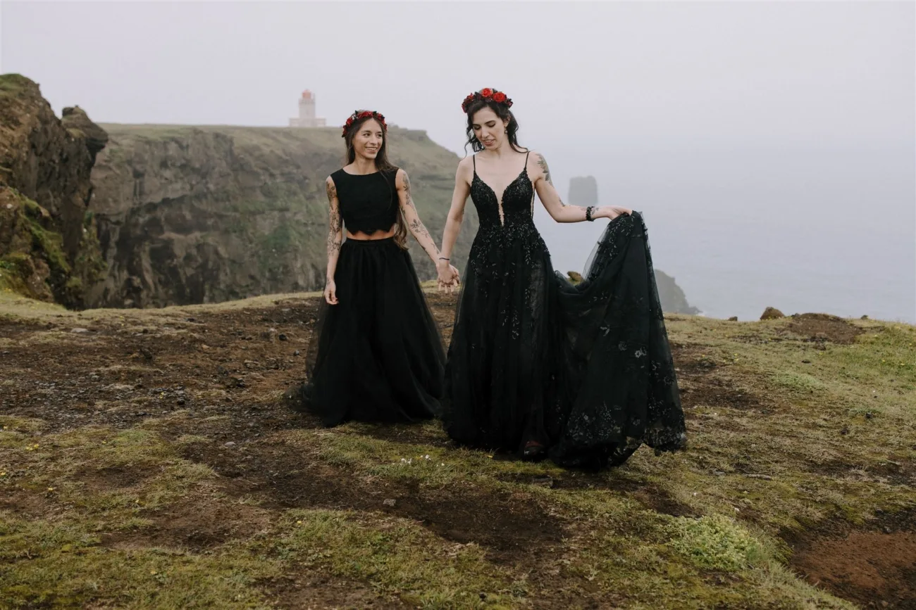 Two brides wearing black wedding gowns and red flower crowns.