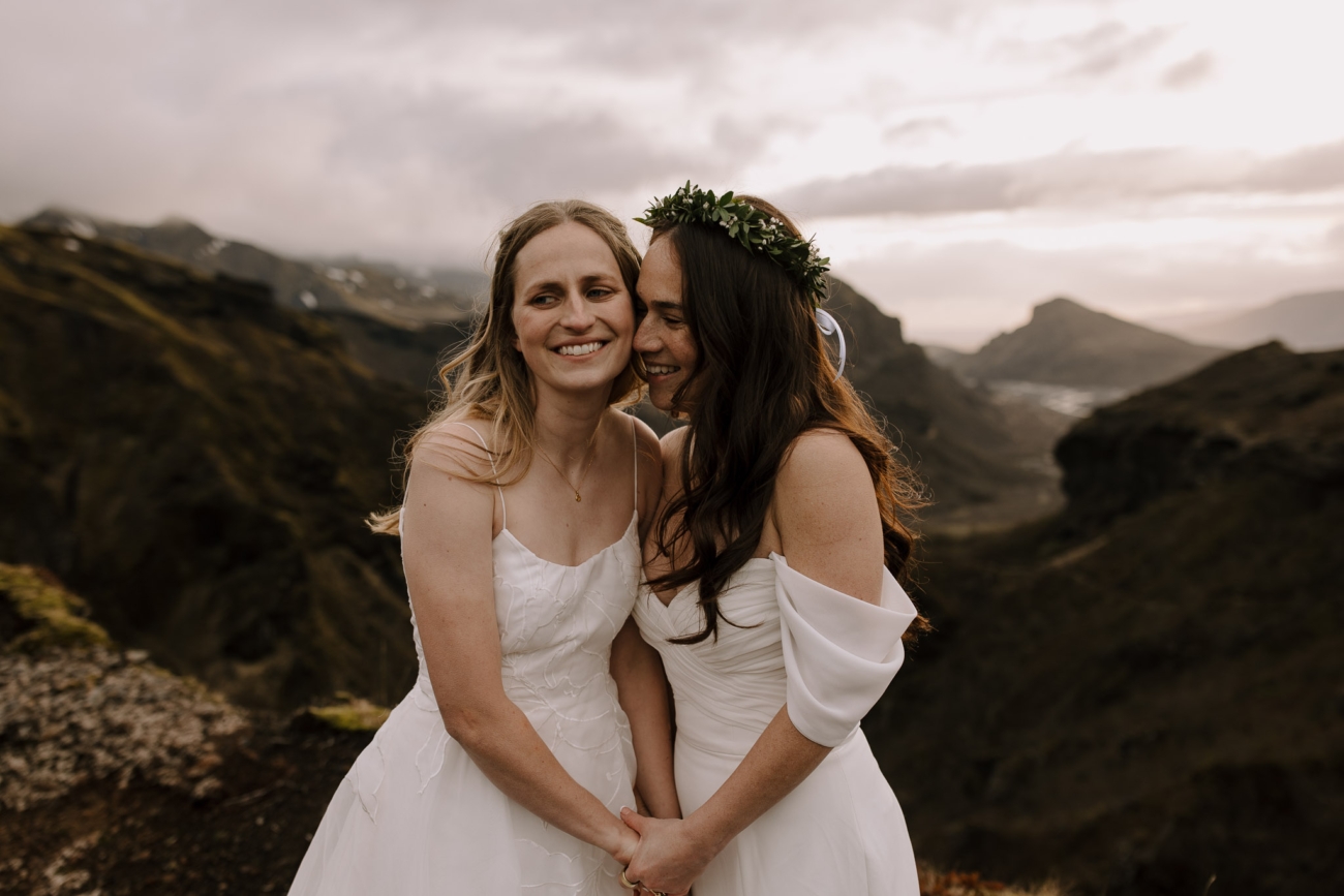 Two brides cuddling on top of a mountain at sunset.