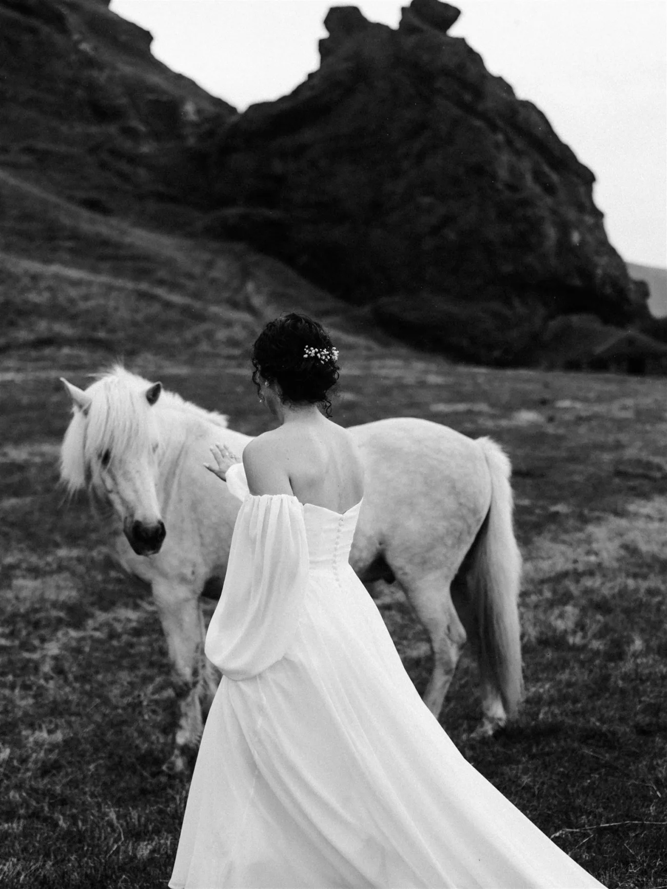 Fairy like scene where a bride in a flowy dress walks up to a white horse