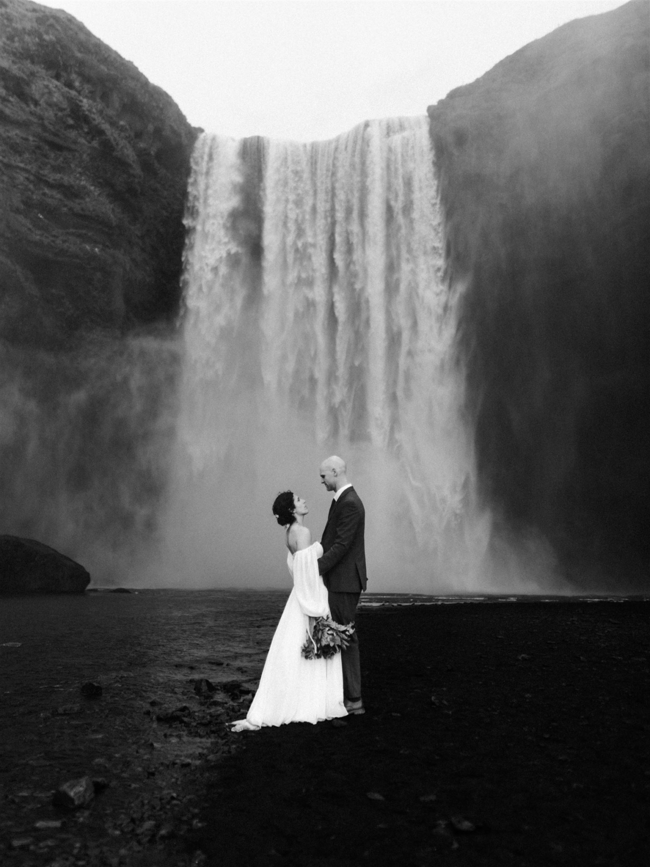 A classic wedding portrait of a couple getting soaked underneath the Skógafoss waterfall during their Iceland elopement.