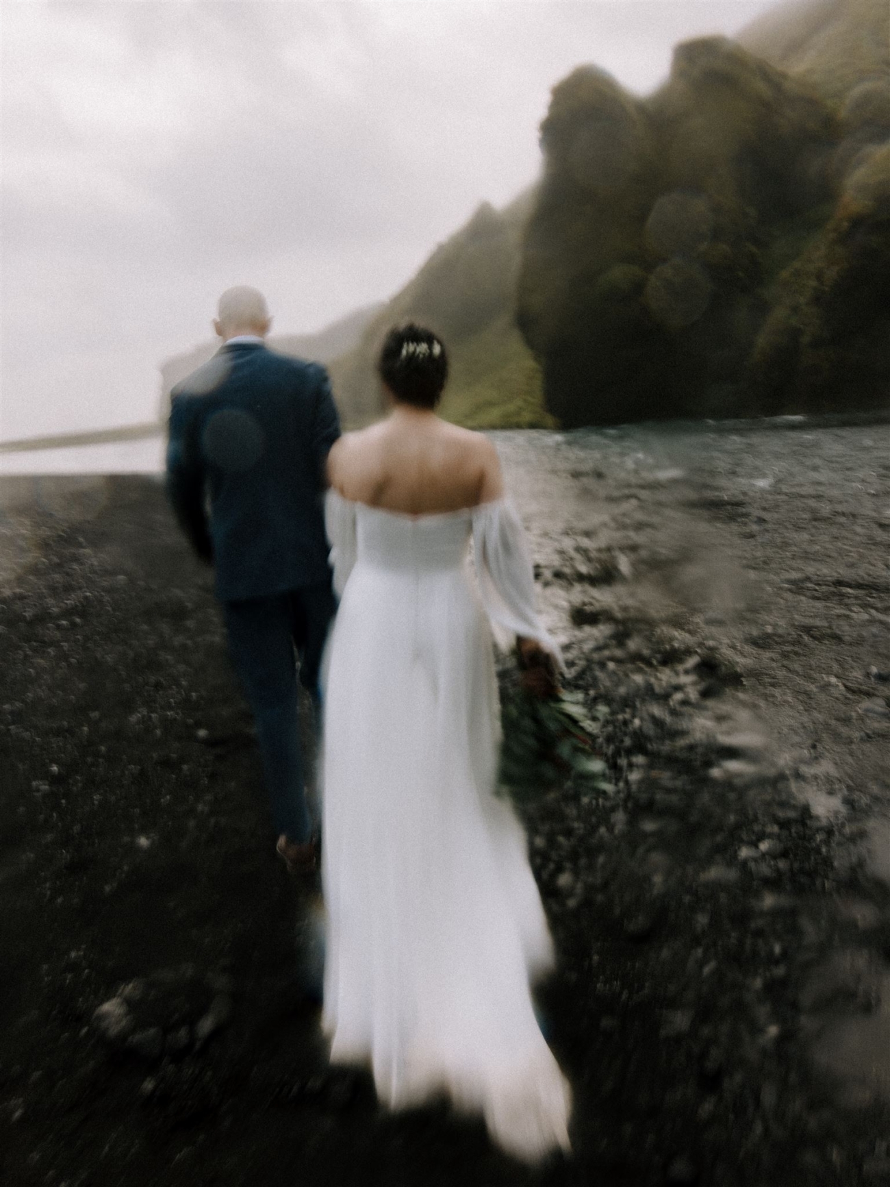 A blurry emotive image of a bride and groom walking through waterfall mist during their Iceland elopement.