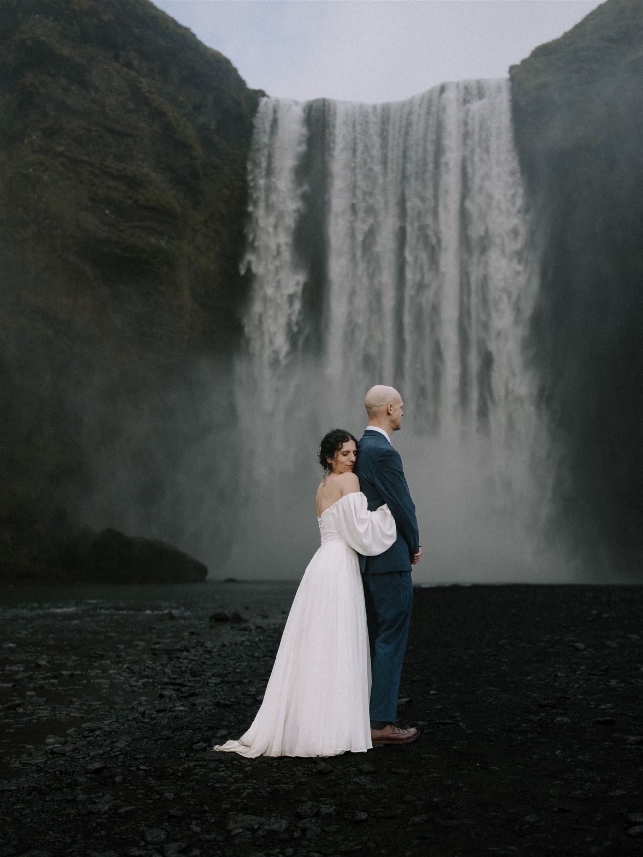 A bride embraces her groom in front of Skógafoss waterfall during their Iceland elopement.