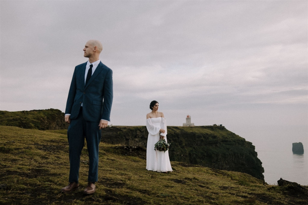 A wedding couple standing and admiring the views over the black sand beaches of south Iceland.