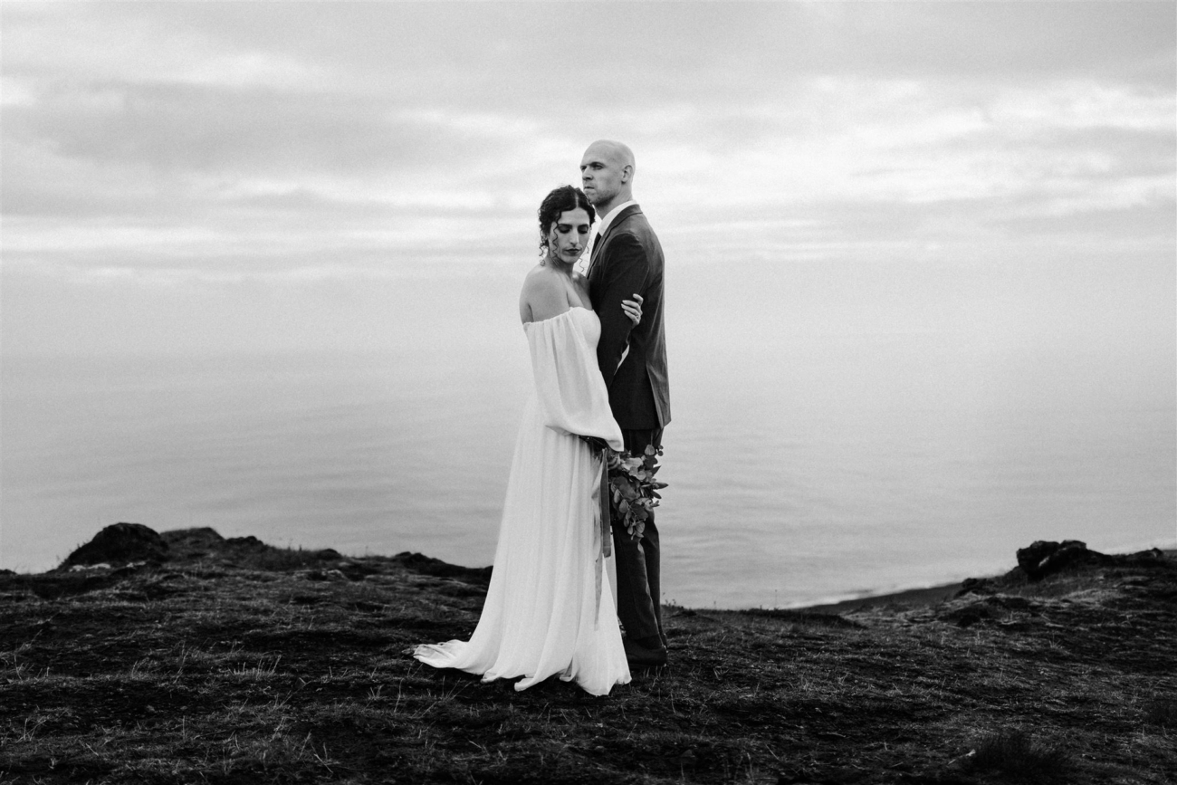 A calm, serene portrait of a bride and groom standing at the edge of a cliff with the Atlantic stretching out endlessly behind them.