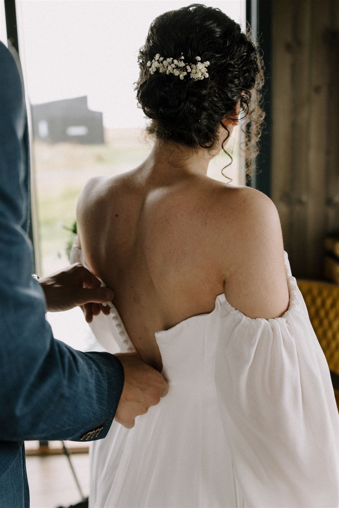 A groom zips up the wedding dress for his bride to be on their Iceland elopement day.