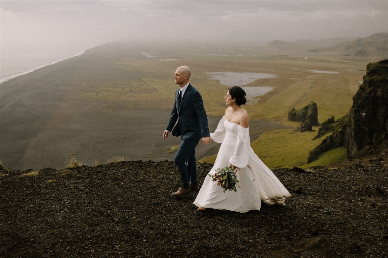 A bride and groom walk along a cliff edge on the south coast during their Iceland elopement day.