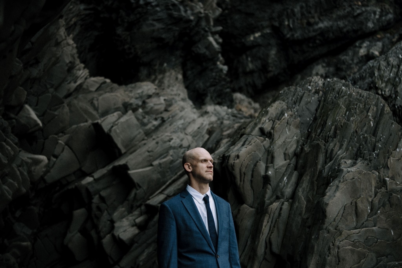 A portrait of a groom with basalt rock formations in the background.