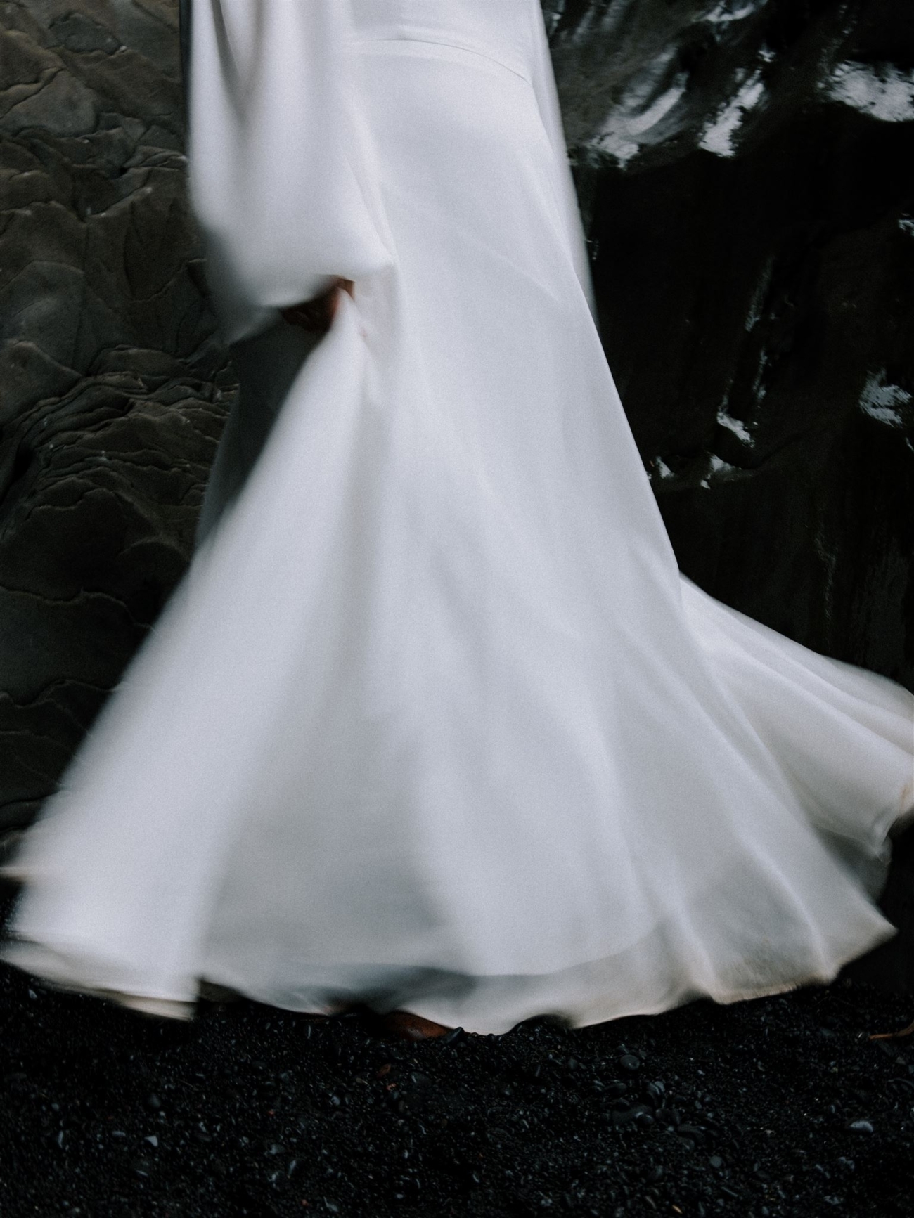 A wedding dress sweeps along the black sand during an Iceland elopement.
