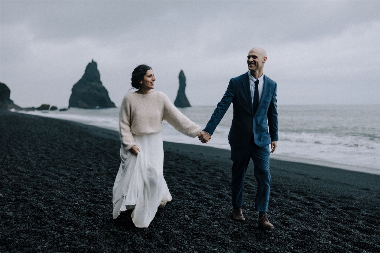 Hand in hand, strolling along the black sand beach on their Iceland elopement day.