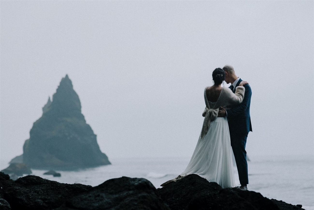 A wedding couple facing the sea stack of Reynisfjara - the black sand beach.