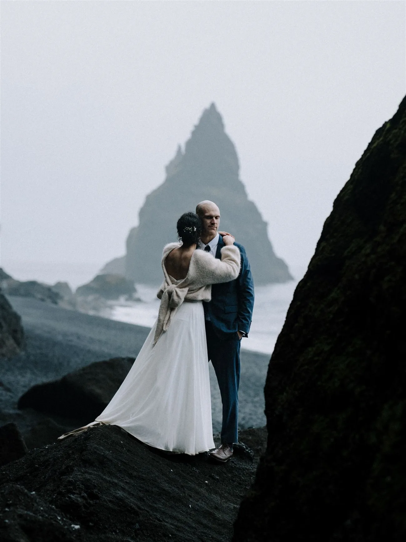 Bride and groom walking on a black beach, the bride wearing a hand knitted wedding sweater.