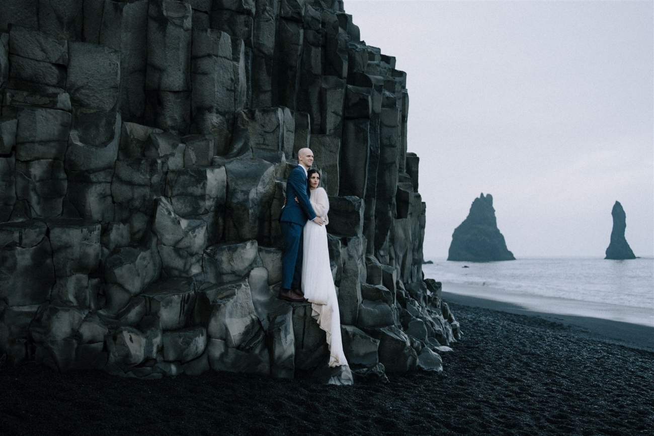 A wedding portrait on the basalt columns of the black sand beach. The columns glistening with newly fallen rain.