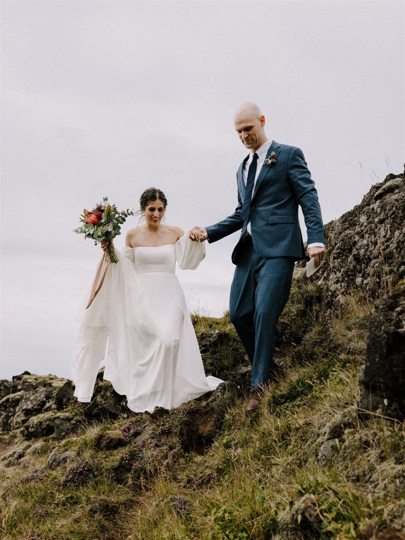 A couple hiking down a steep slope to reach the secret waterfall during their Iceland elopement ceremony.