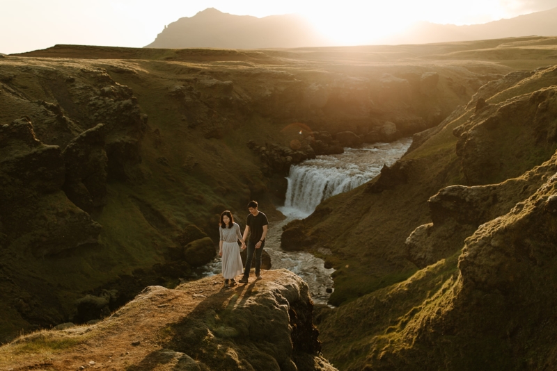 A couple standing in front of a hidden waterfall in the golden sun.