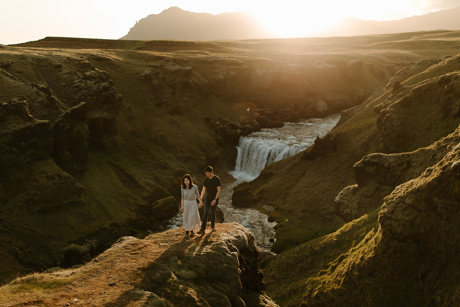 A couple standing in front of a hidden waterfall in the golden sun.