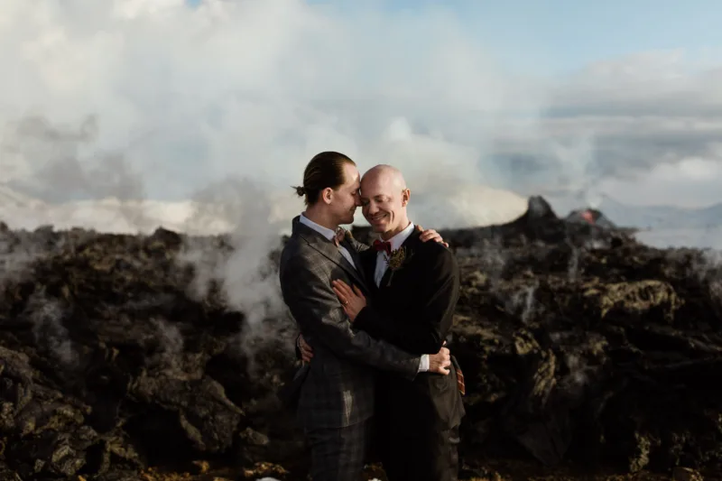 A couple poses in front of a lava stream coming from an active volcanic crater in Iceland.