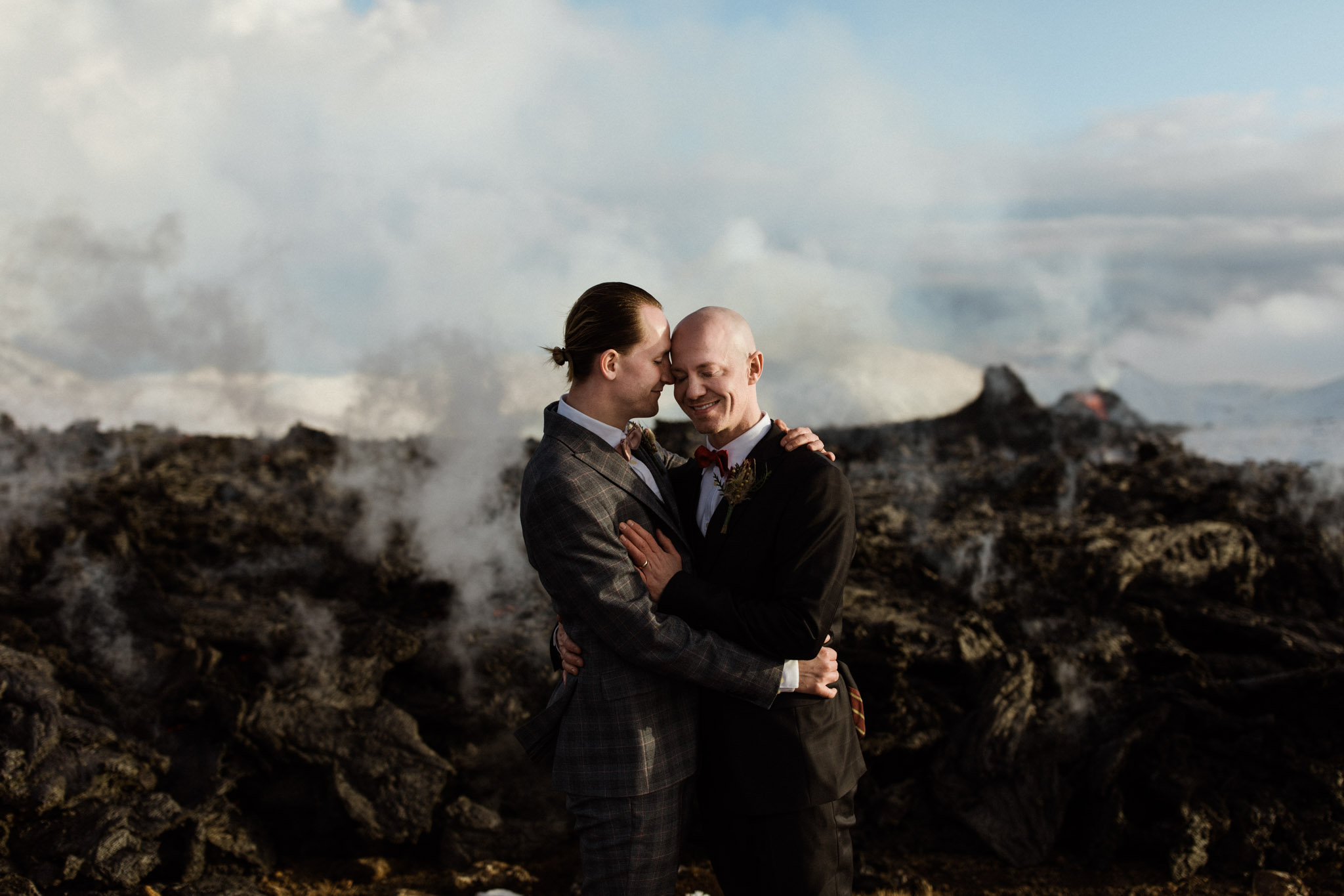 A couple poses in front of a lava stream coming from an active volcanic crater in Iceland.