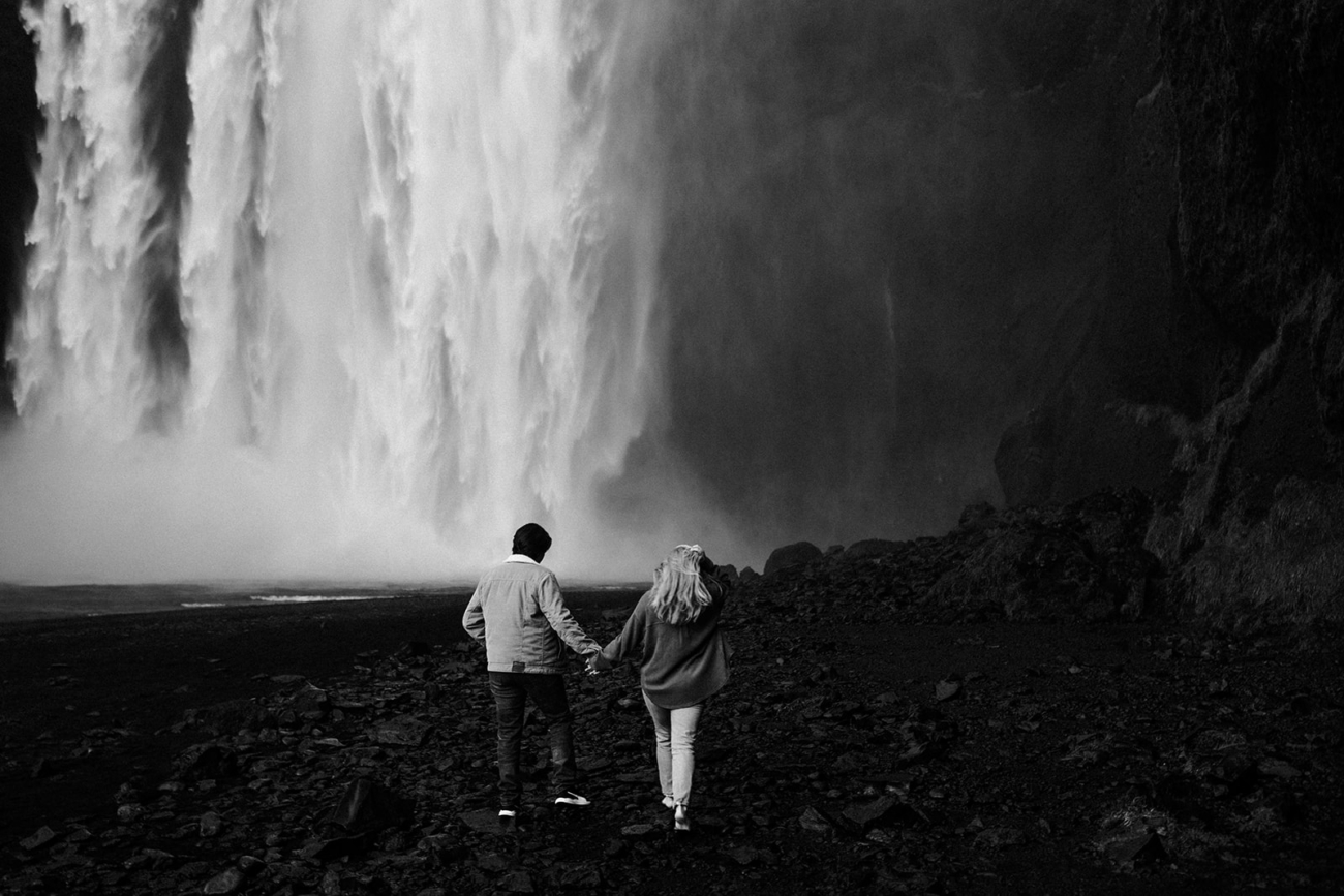A black and white image of the couple running towards the big waterfall in the background.