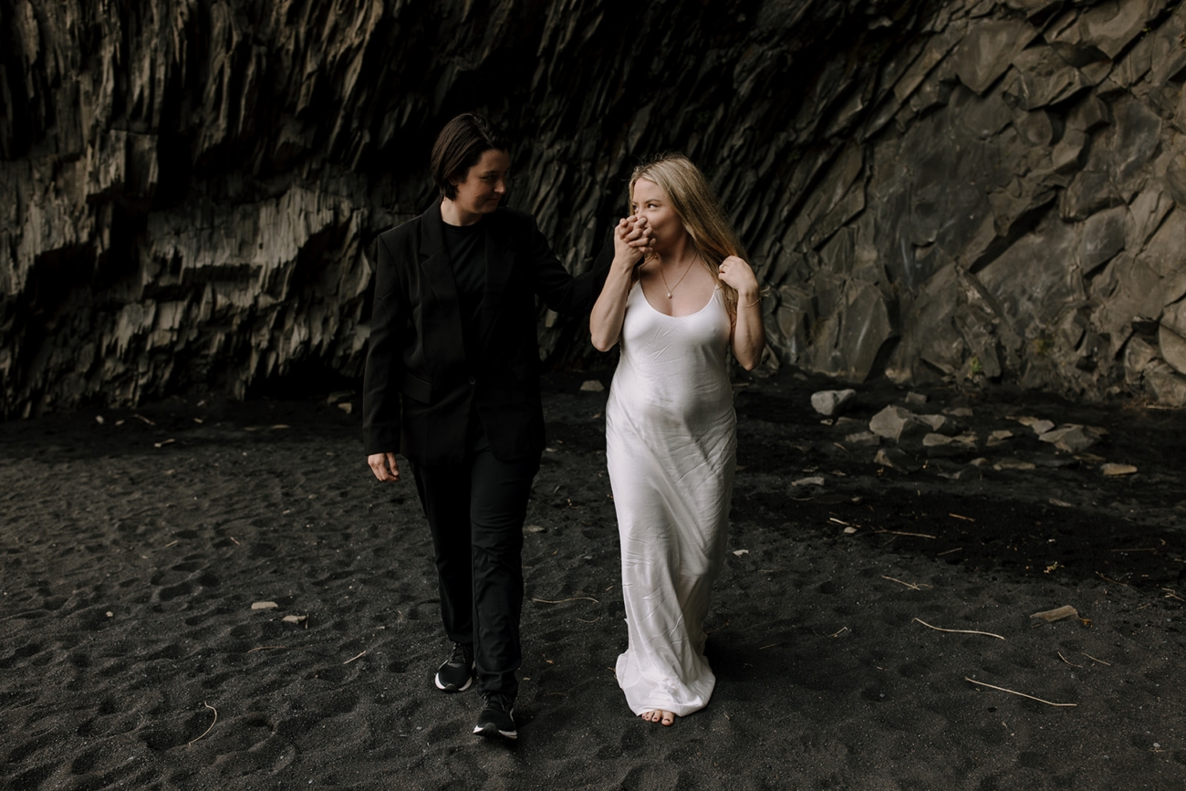 A lesbian couple walking bare foot on a black sand beach.