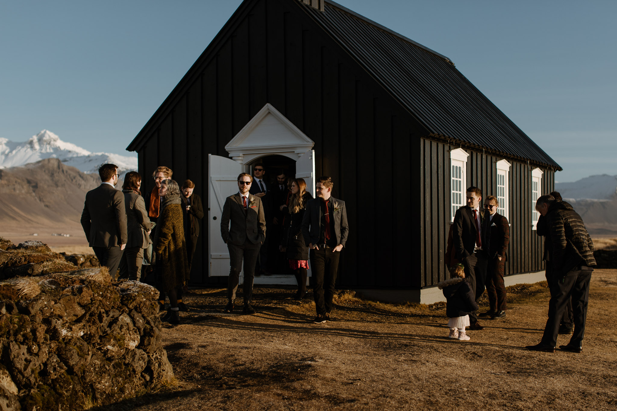 Wedding guests standing out side the black church at Búðir during a Iceland destination wedding ceremony.