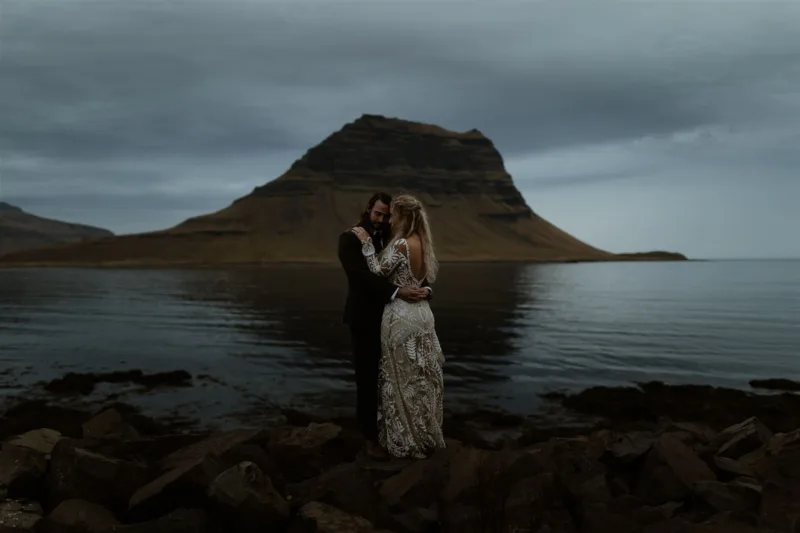 A couple in a warm embrace at dusk in front of the Kirkjufell mountain in Iceland.