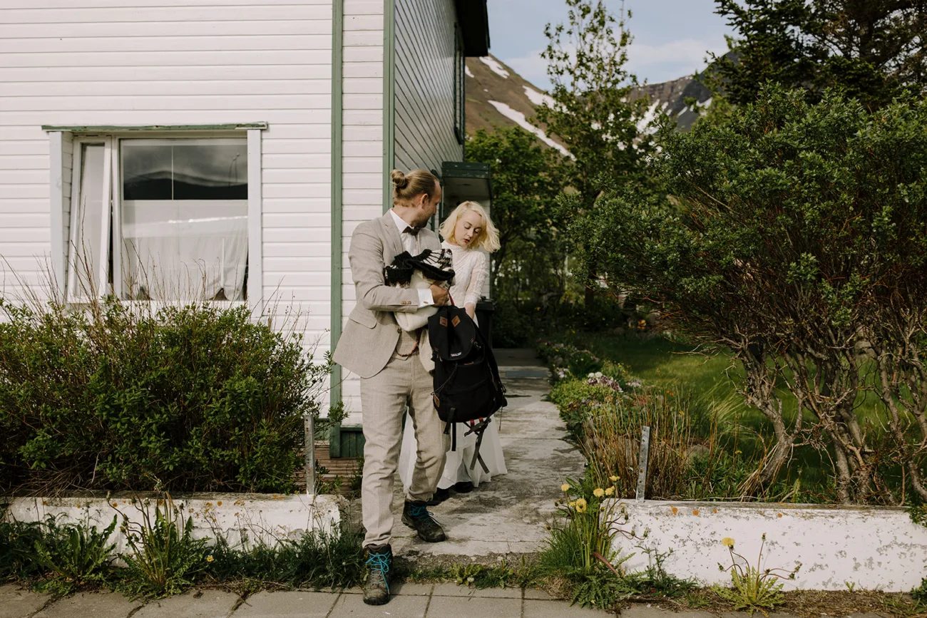 Bride and groom caring backpacks walking out the door of their getting ready accommodation.