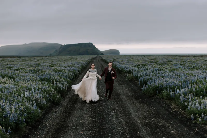 Bride and groom running through lupin field, bride wearing a wool sweater