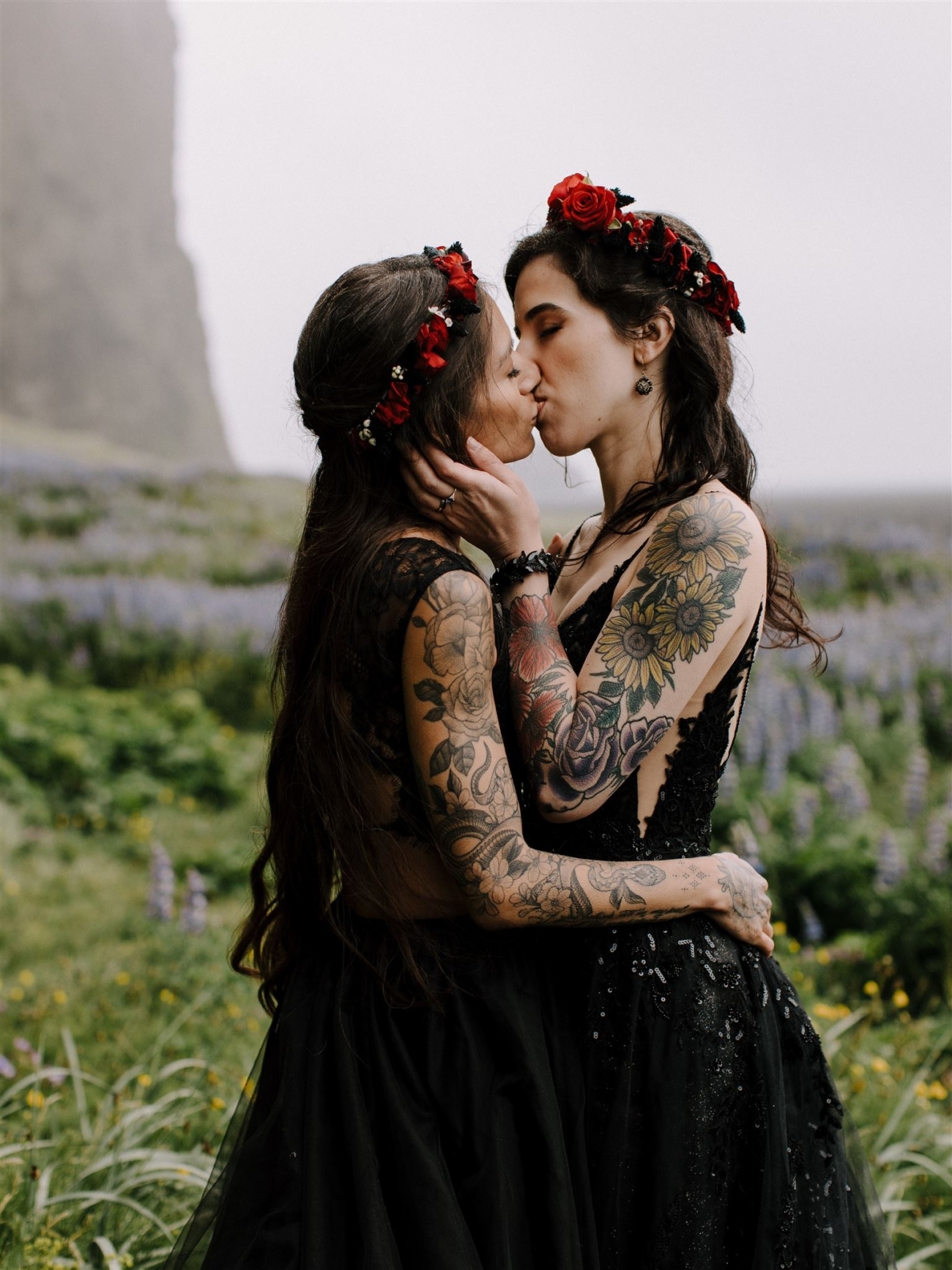 Two heavily tattooed brides kissing on a rainy day in Iceland.