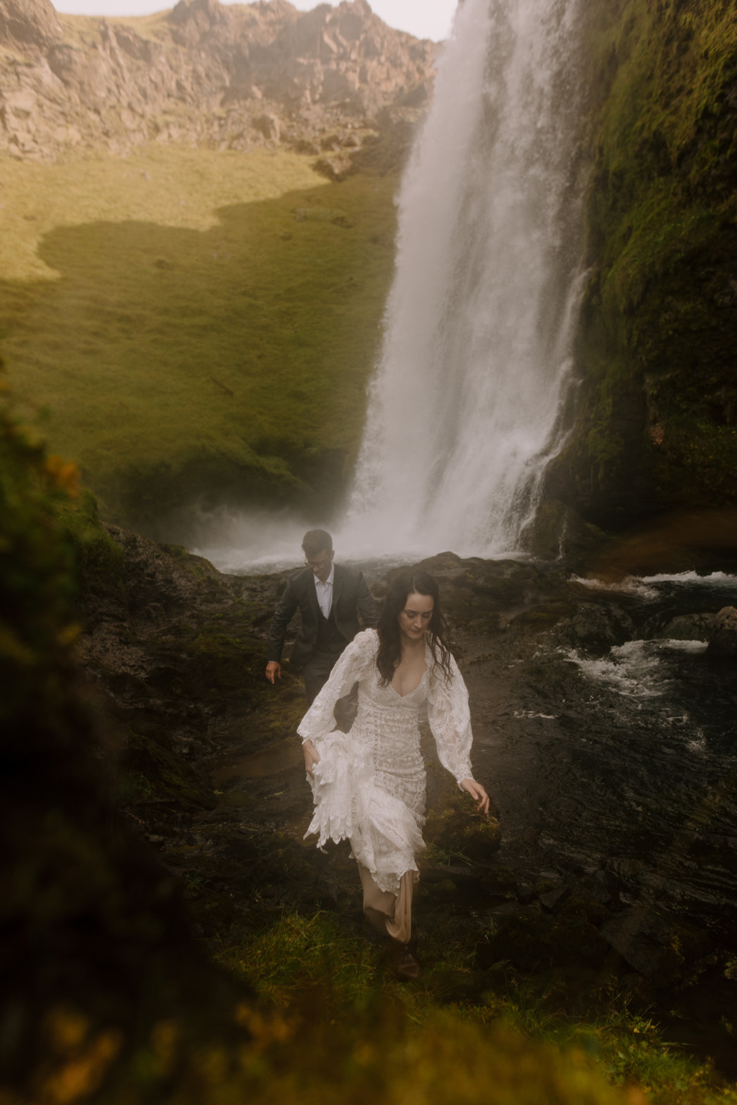 A bride hiking back from a waterfall, soaked in the spray from the falling water.