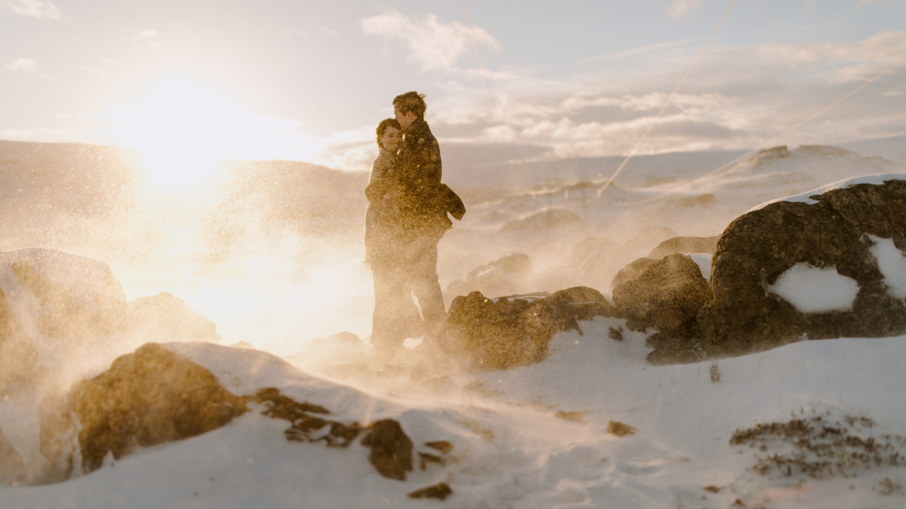 A couple stands in a snow drift illuminated by the low winter sun.