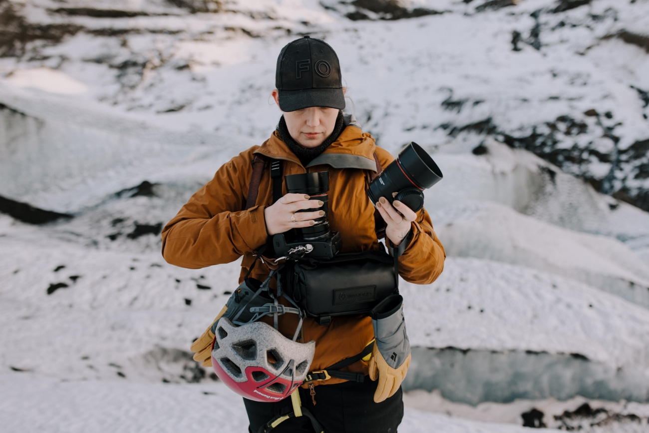 A photographer switching lenses on top of a glacier on assignment, photographing an adventure elopement.