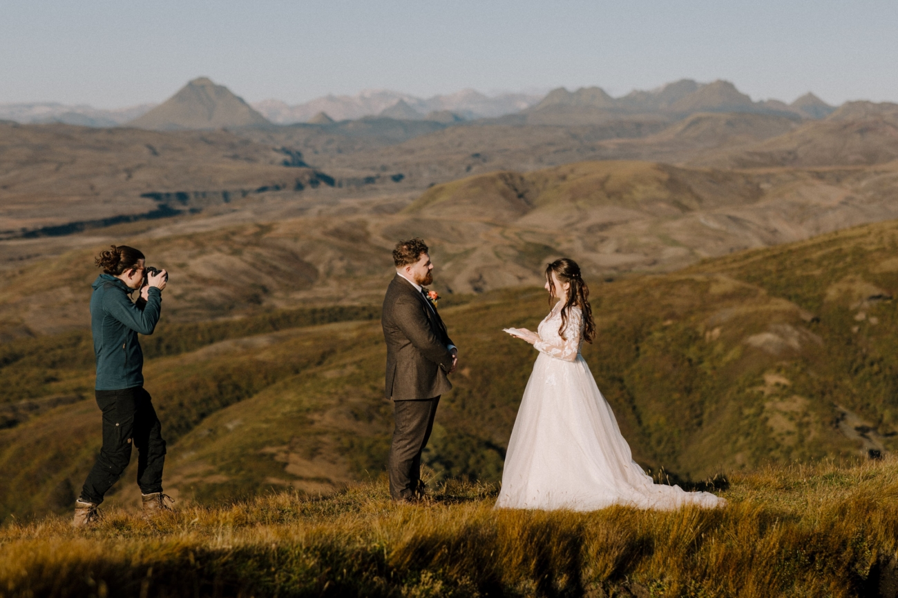 An elopement photographer in the wild, taking photos of a couple reading vows on top of a mountain in the highlands.