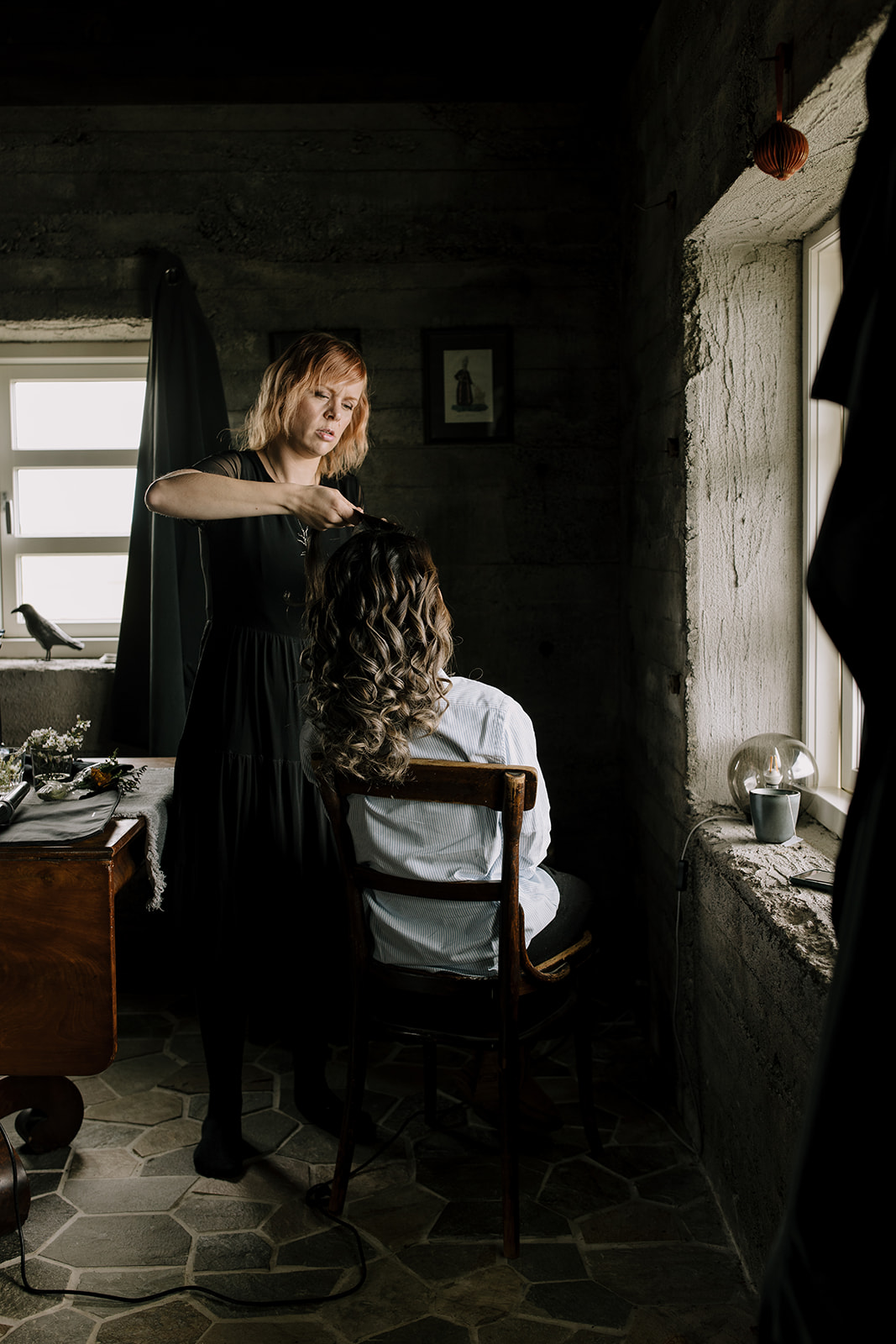 A hair and make up artist working her magic on a brides hair in a moody little cabin in Iceland.