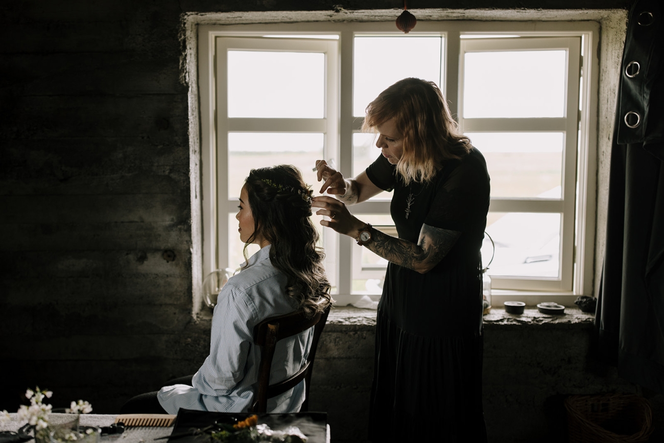 A hair and make up artist working her magic on a brides hair in a moody little cabin in Iceland.