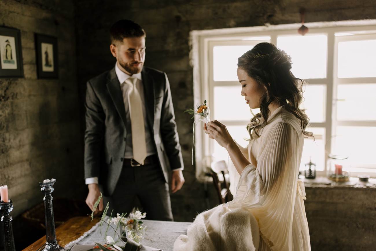 A bride puts a boutonniere on the groom as a finishing touch to their getting ready.  