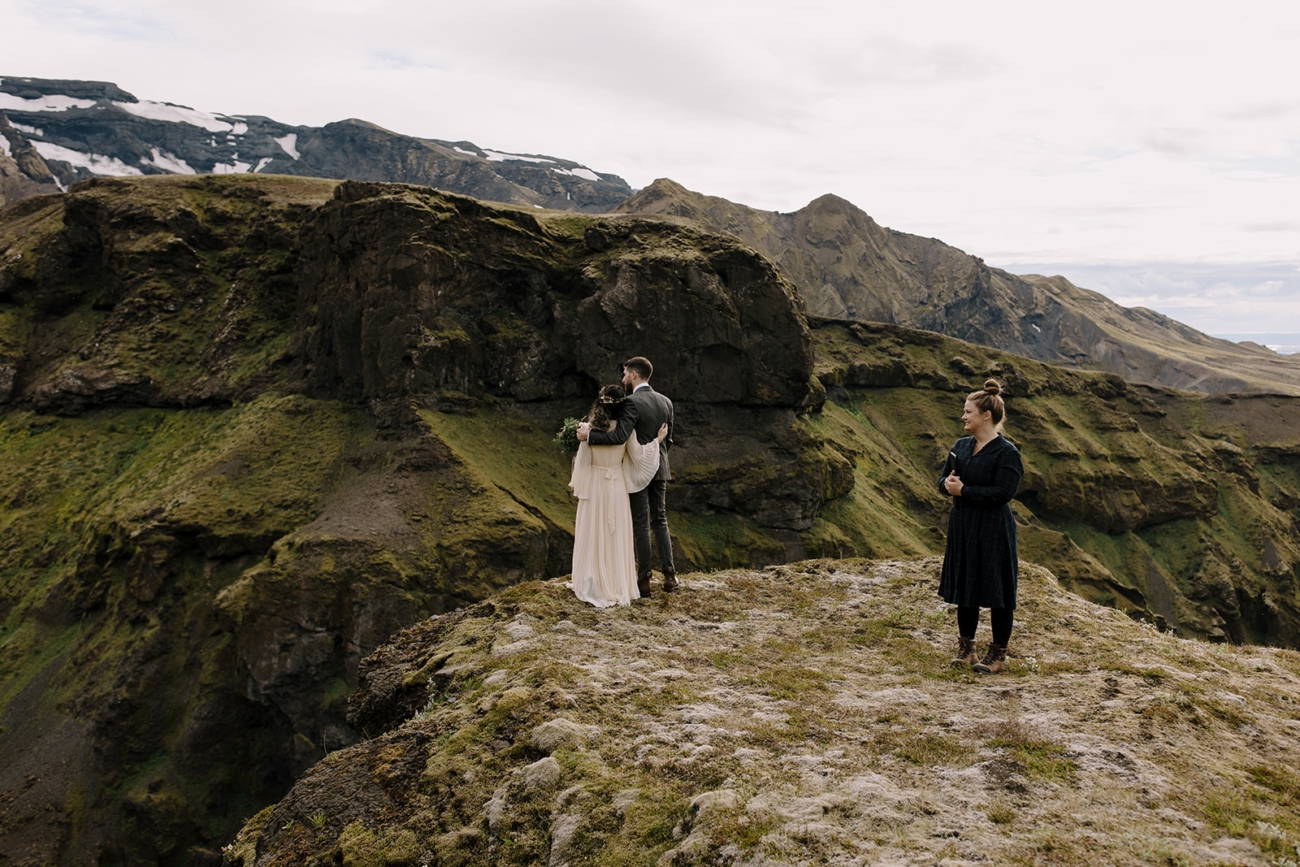 A couple admires the view of their elopement ceremony spot as the officiant patiently waits for them.