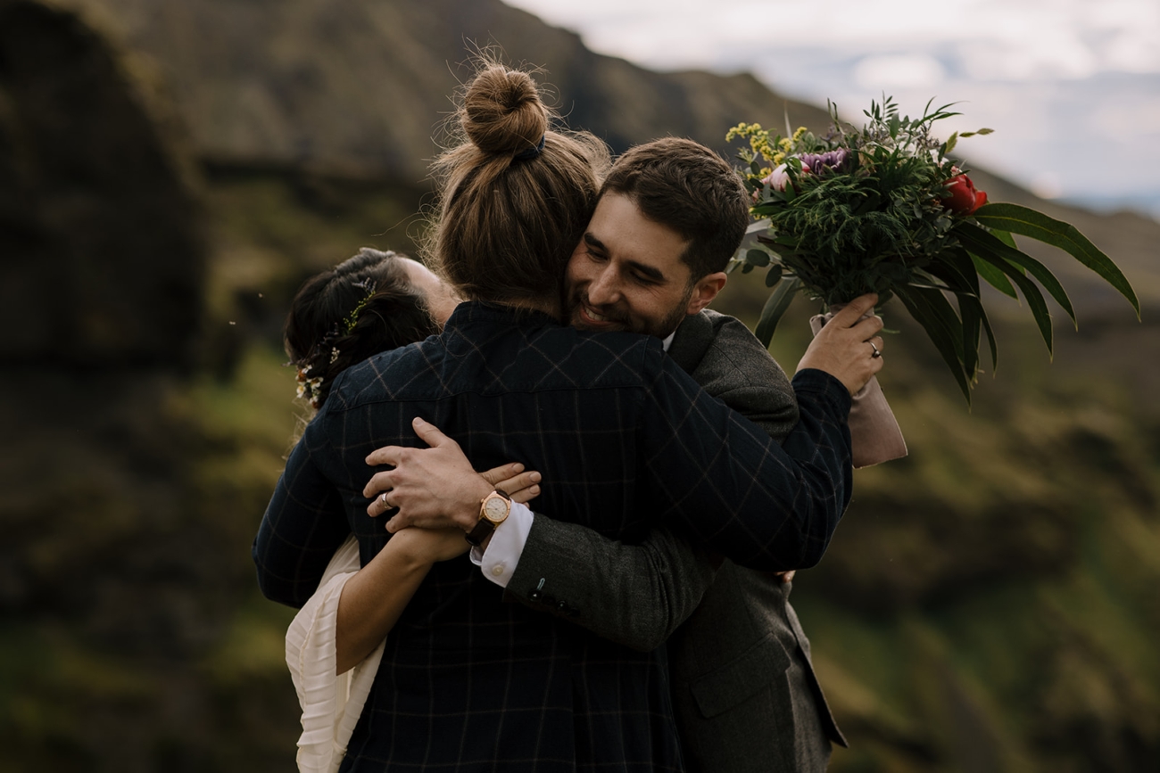 A couples passionately embrace their wedding officiant after their ceremony overlooking a mossy canyon in Þórsmörk. 