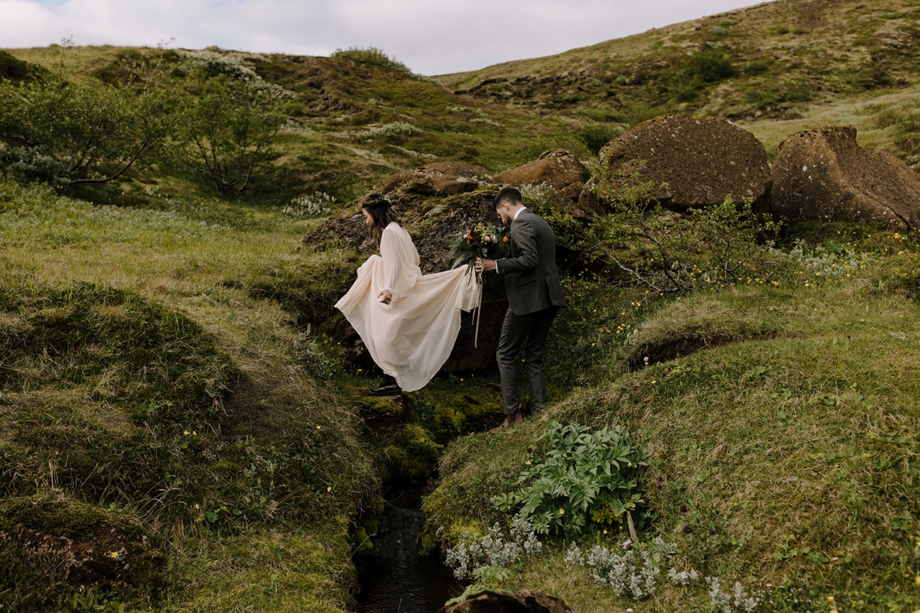 Whimsically crossing small streams in wedding attire.