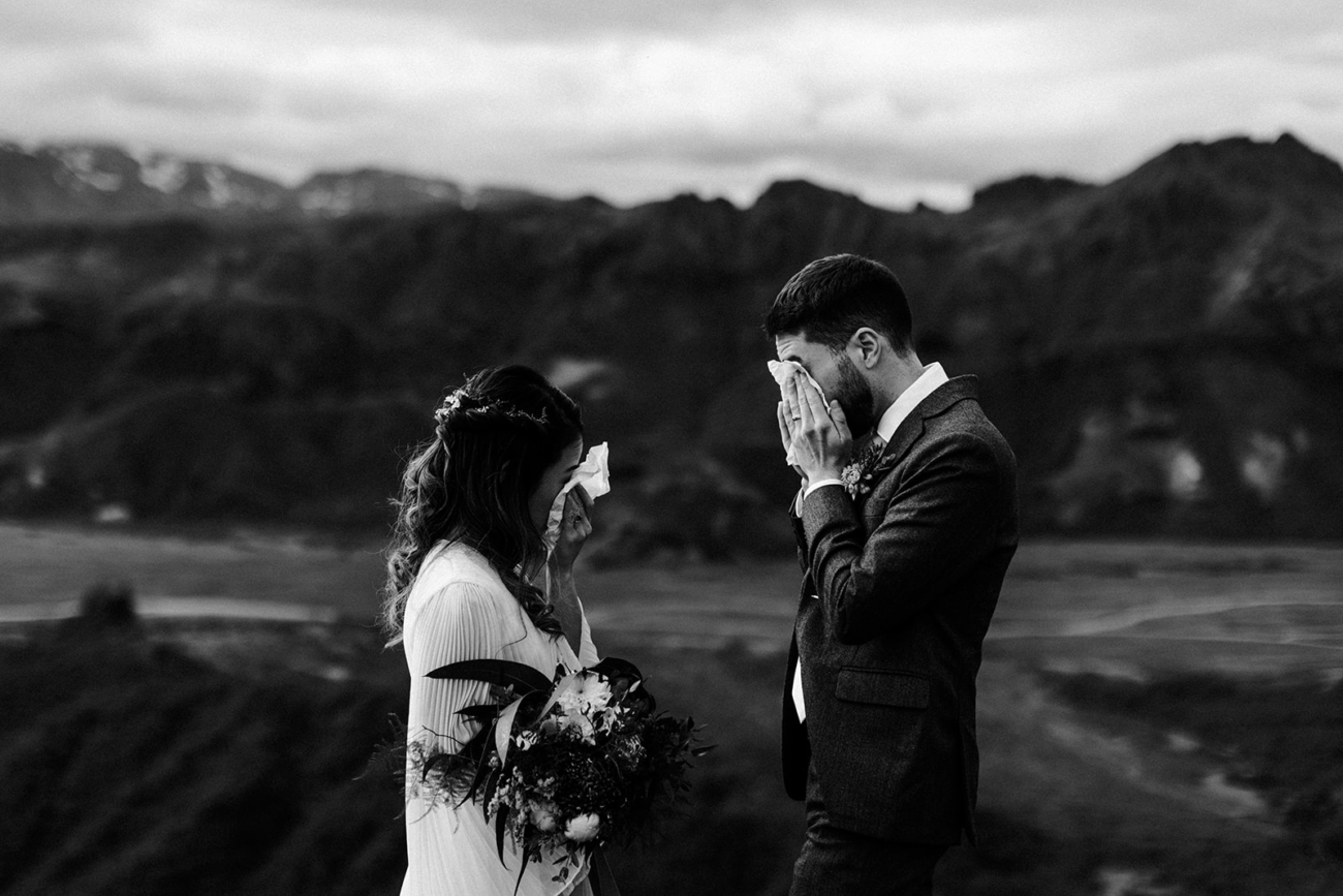A bride and groom both wipe away tears after reading personal vows. 