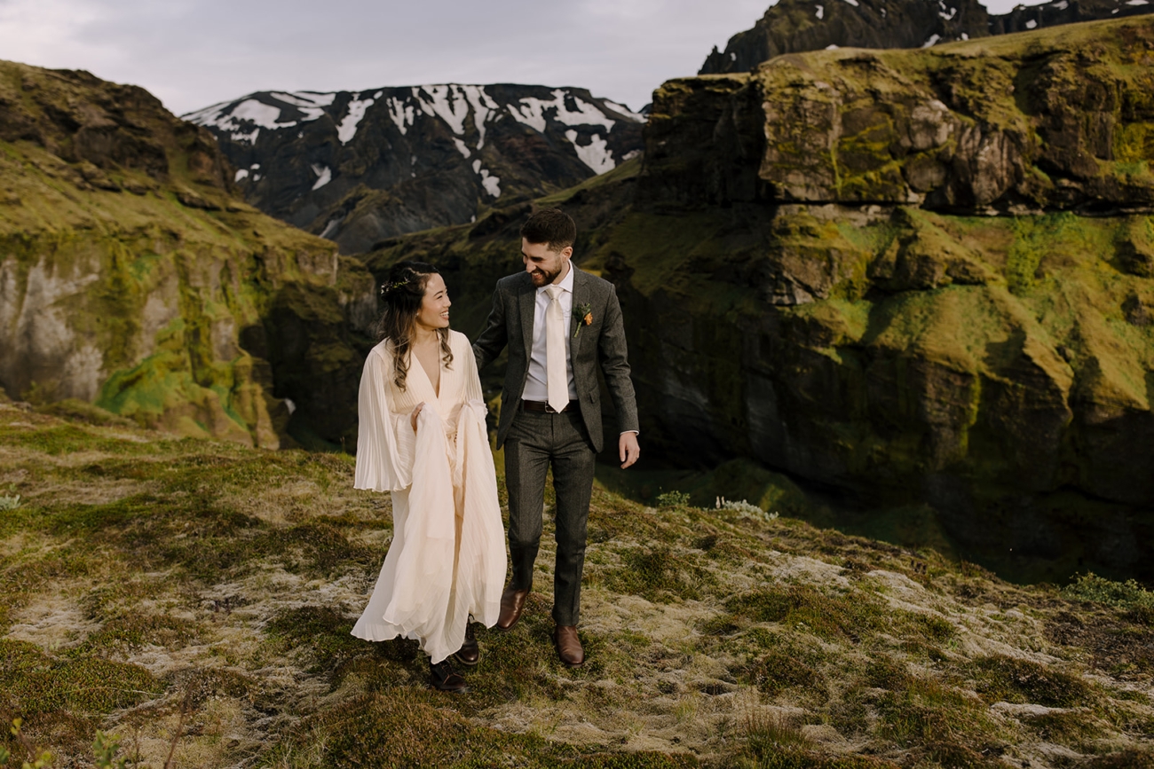 A wedding couple hikes in green mountain landscapes in Iceland.