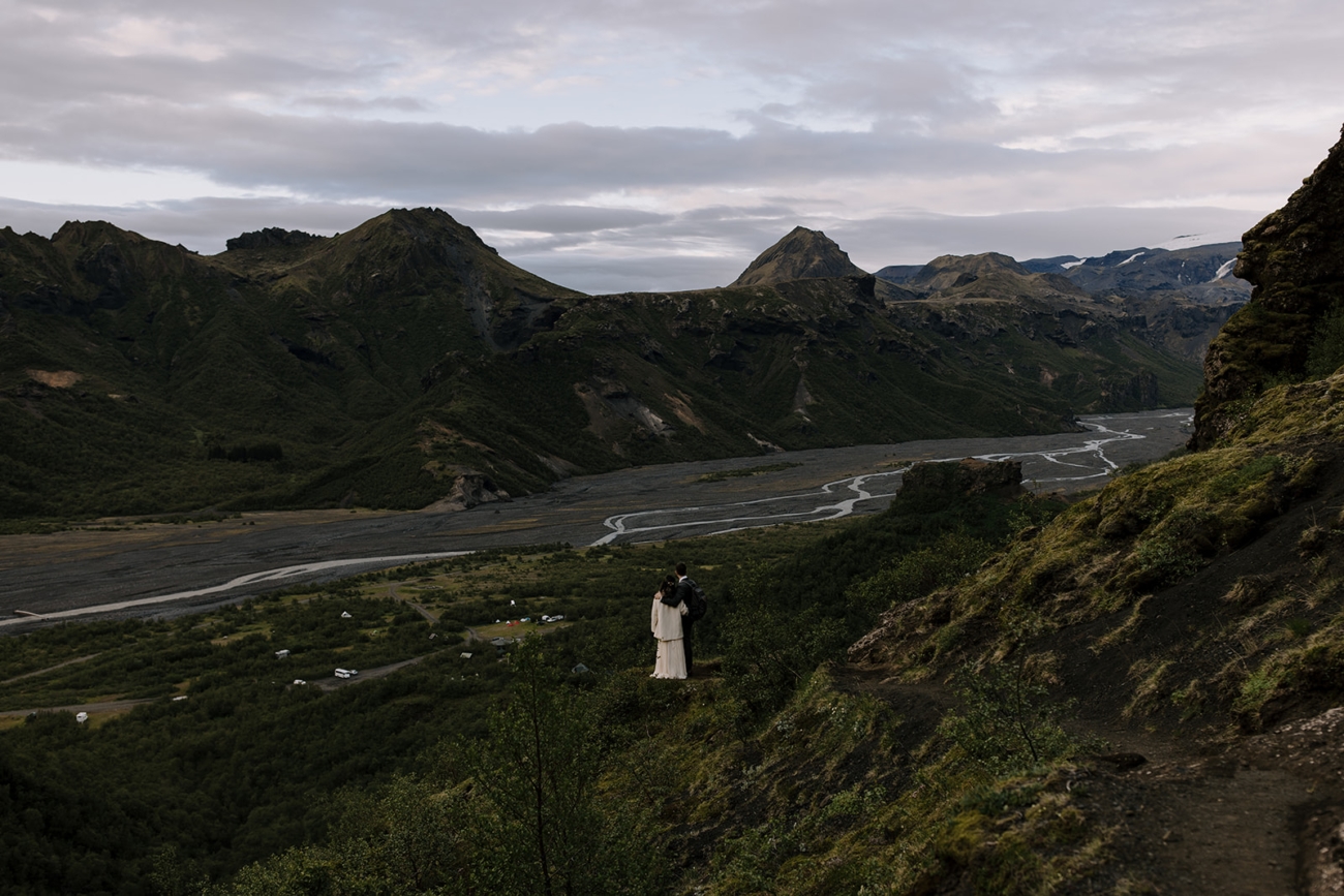 A couple stand at the edge of a trail over looking the river valley of Þórsmörk, as they head back down after their intimate wedding ceremony.